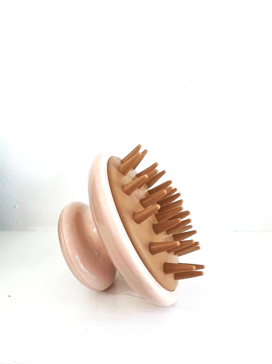 A bronze colored head massager made of plastic, round with long bristles.